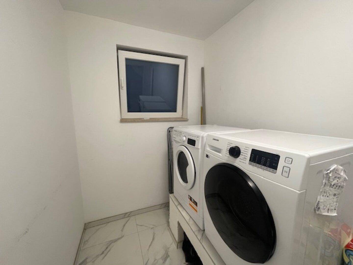 Praktischer Hauswirtschaftsraum mit Waschmaschine, Trockner und Fenster.