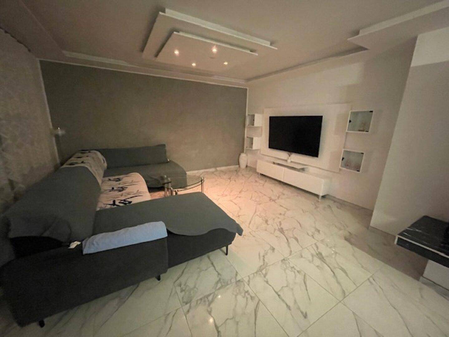 Geräumiges Wohnzimmer mit großem Sofa, Fernseher und elegantem Fliesenboden.