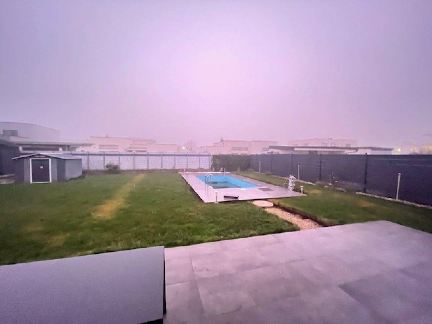 Großer Garten mit Swimmingpool, Rasenfläche und Gartenhaus an einem nebligen Tag.