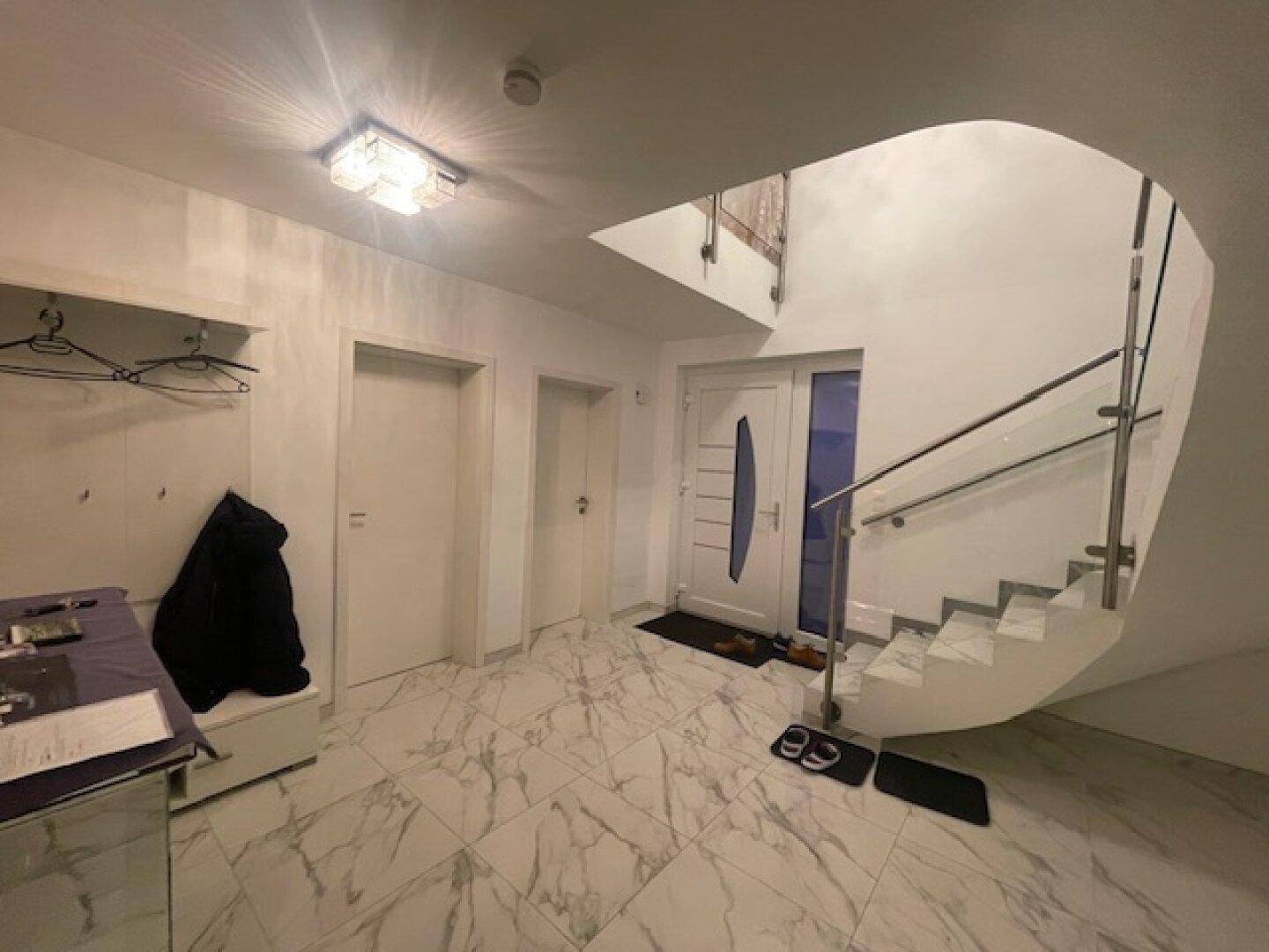 Heller Eingangsbereich mit moderner Treppe, Garderobe und Fliesenboden.