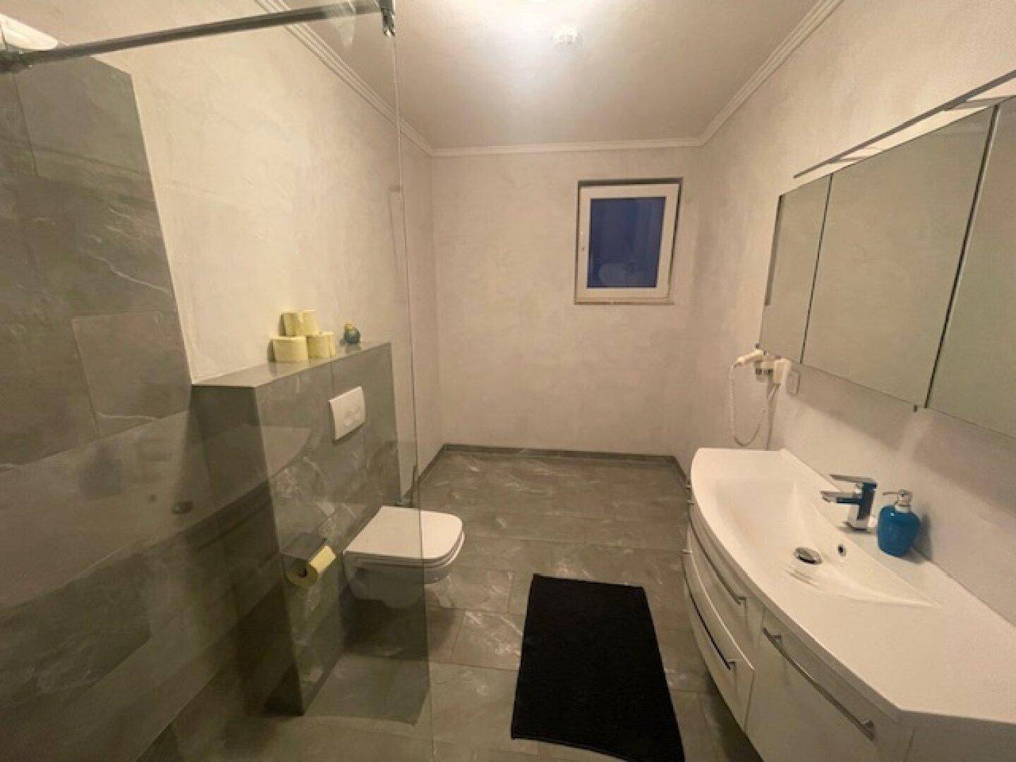 Modernes Badezimmer mit Dusche, Wand-WC, Doppelwaschbecken und Fenster.