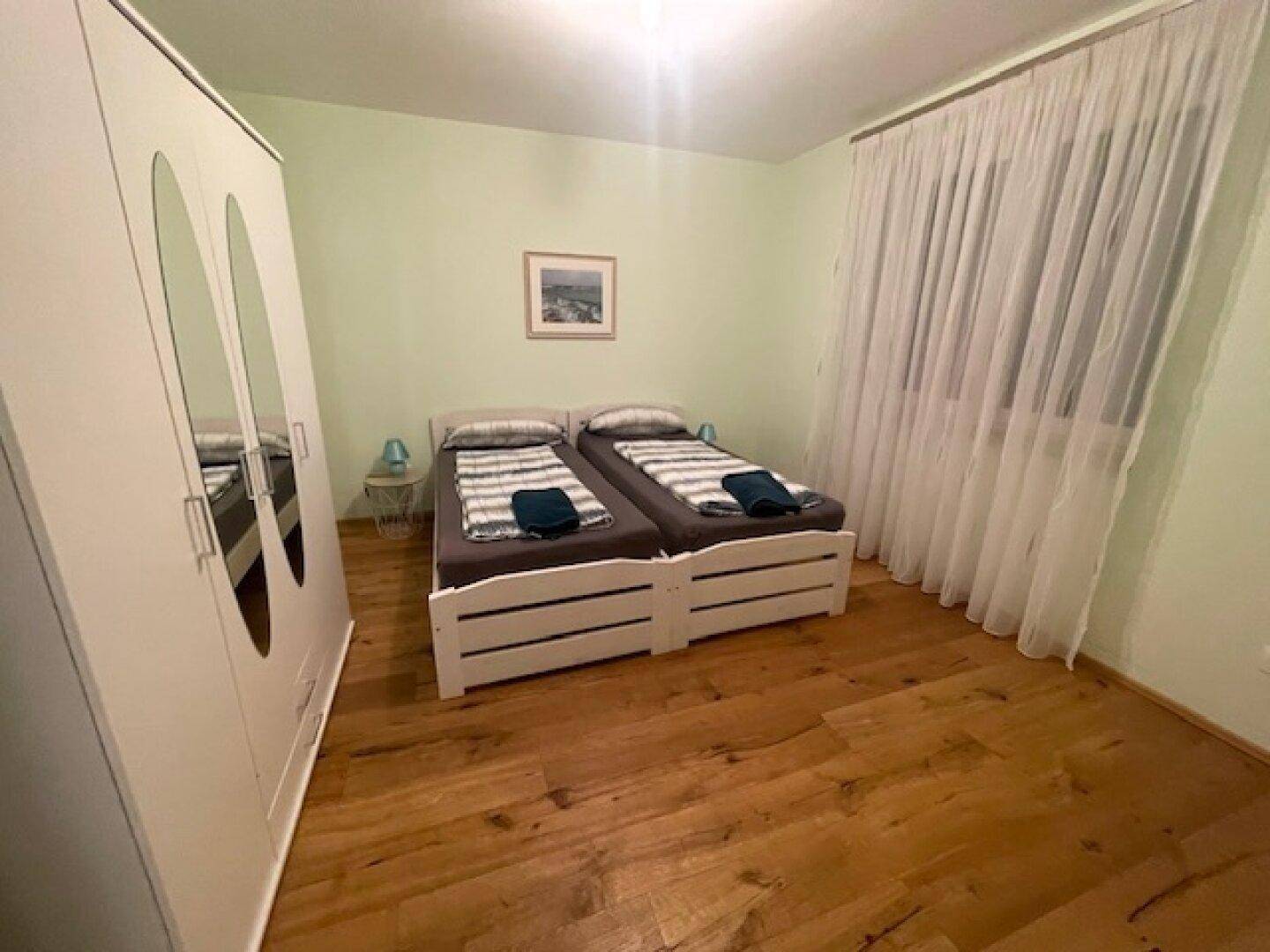 Helles Schlafzimmer mit zwei Einzelbetten, Kleiderschrank und Holzparkett.