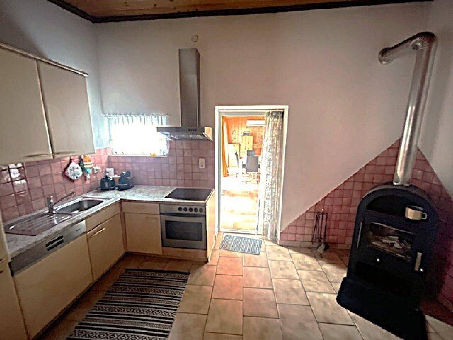 Funktionale Küche mit Einbauschränken, Fliesenboden und einem Holzofen für zusätzliche Wärme.