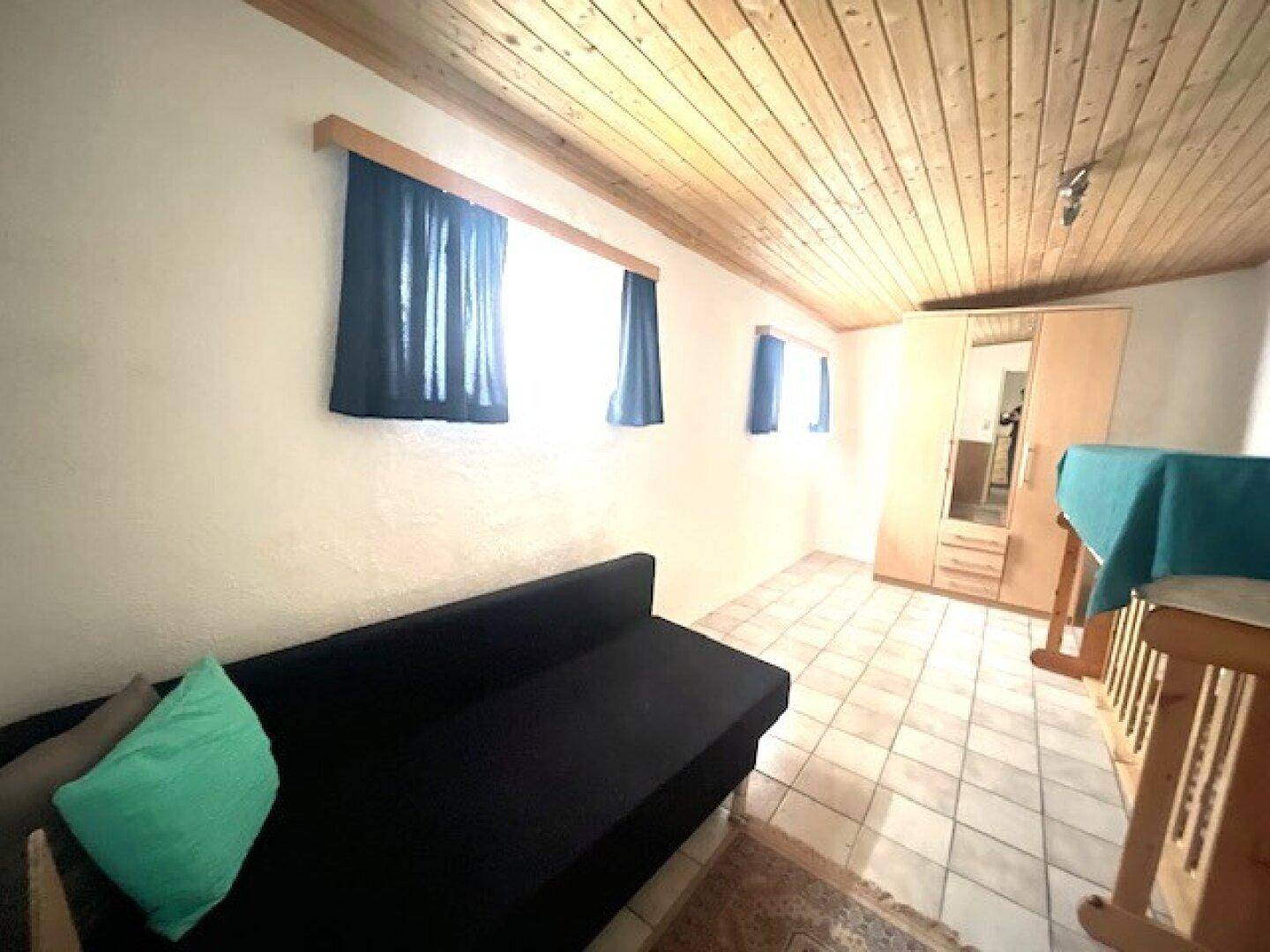 Schlafzimmer mit Holzbalkendecke, Fliesenboden, Schlafsofa und Kleiderschrank.
