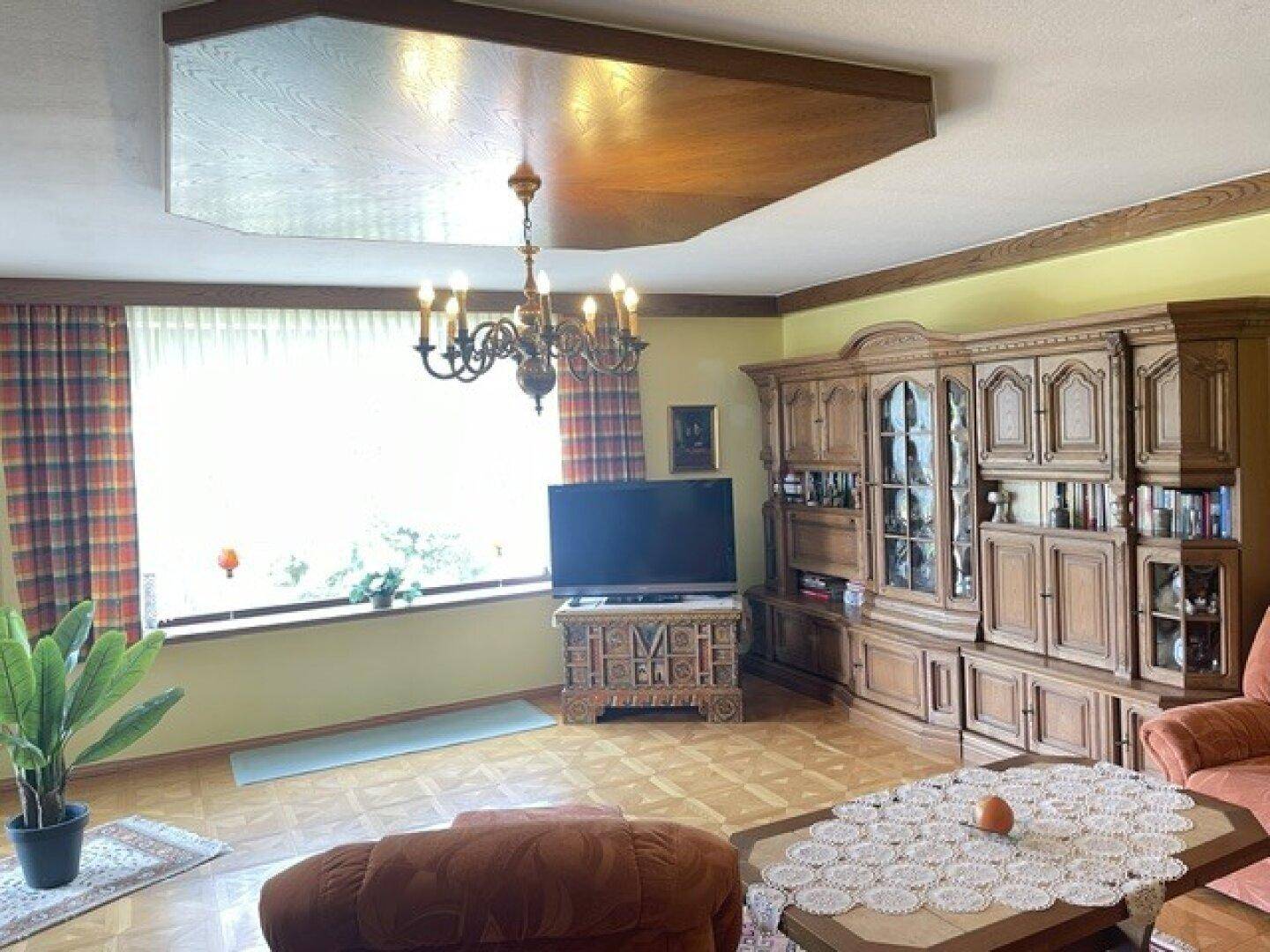 Traditionelles Wohnzimmer mit Holzdecke, Parkettboden und großem Fenster mit Blick ins Grüne.