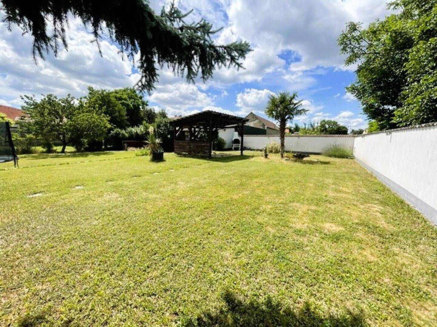 Großer, gepflegter Garten mit Rasenfläche, Palmen und einer Holzgartenlaube mit Grillplatz.