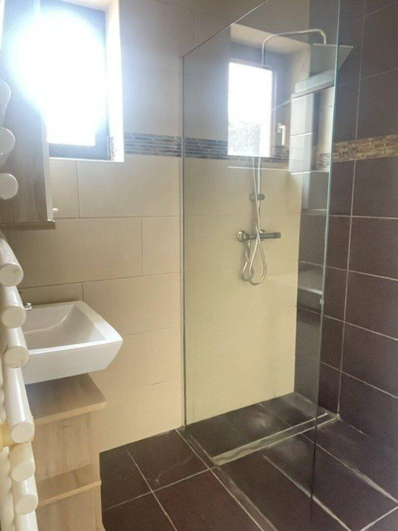 Modernes Badezimmer mit begehbarer Dusche, Fliesen in Beige und Braun sowie einem kleinen Waschbecken.