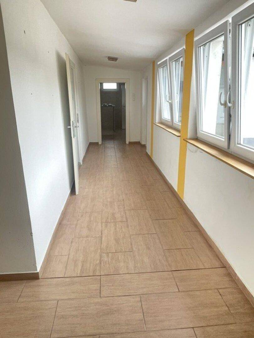 Langer Flur mit Fliesenboden und mehreren Fenstern, die viel Tageslicht hereinlassen.