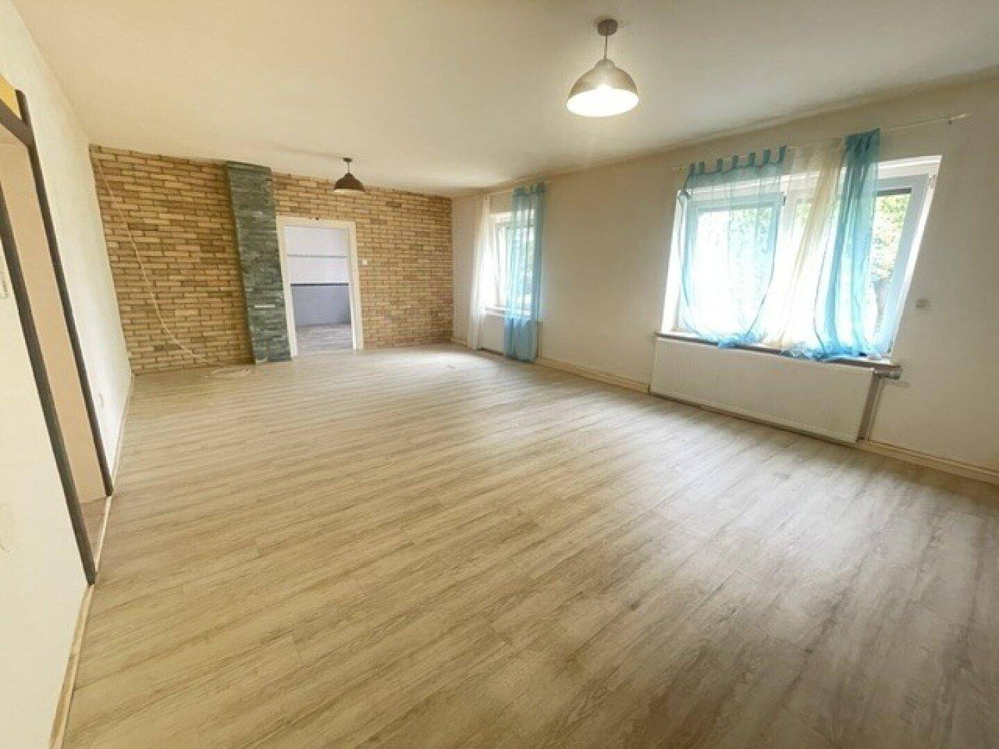 Geräumiges Wohnzimmer mit Laminatboden, weißen Wänden und einer Akzentwand aus Ziegeln.