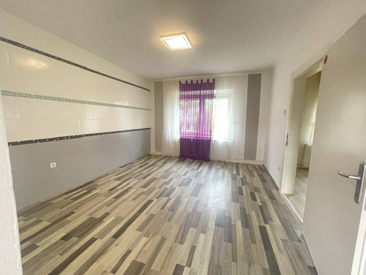 Helles Zimmer mit Laminatboden und dekorativen Streifen an den Wänden, bereit zur Einrichtung.