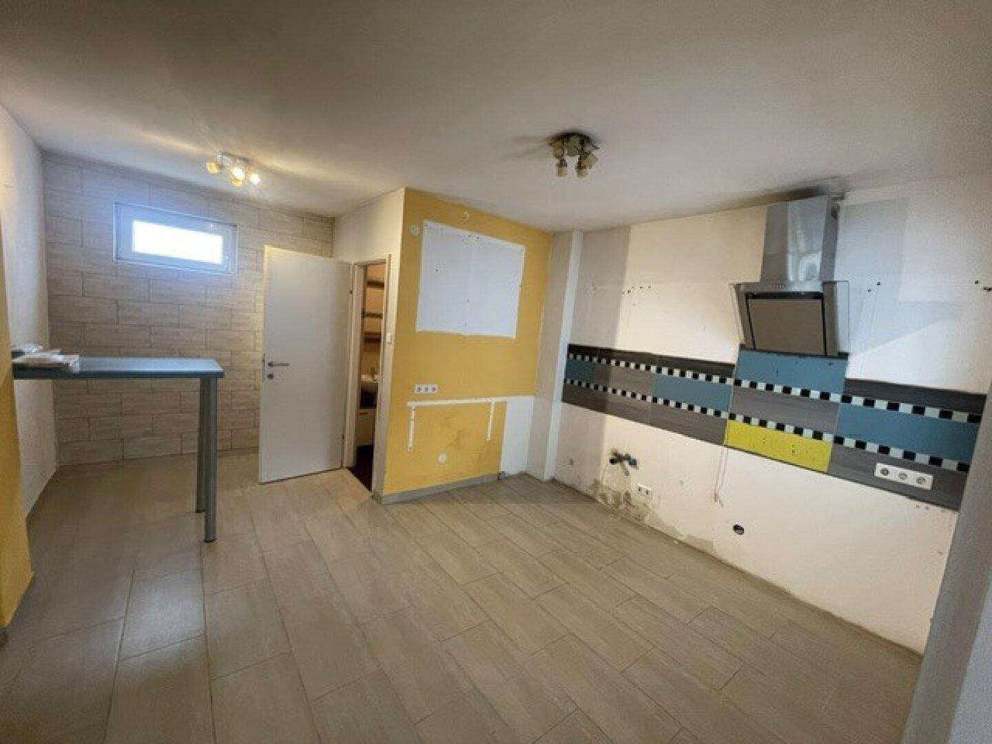 Unfertige Küche mit Fliesenboden, Dunstabzugshaube und gelben Akzentwänden, bereit für Einbauküche.