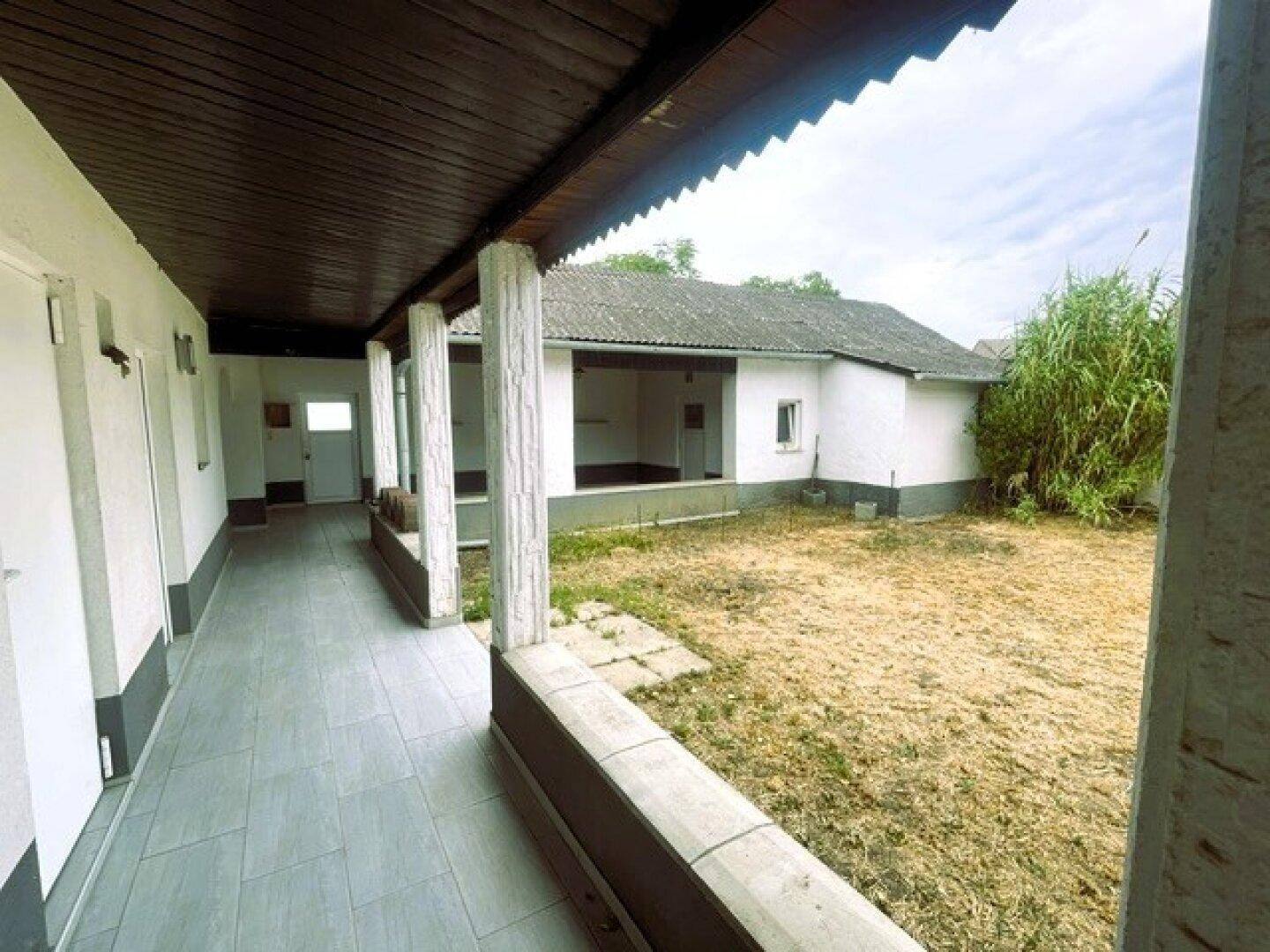 Überdachte Loggia mit Fliesenboden und Säulen, die einen Blick auf den trockenen Gartenbereich bietet.
