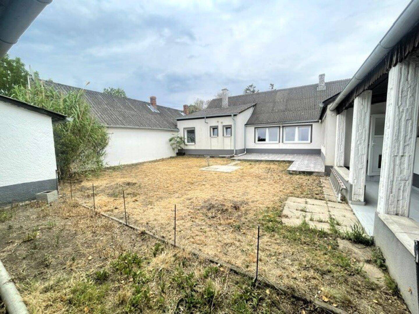 Weitläufiger Gartenbereich mit trockener Rasenfläche und Blick auf das Gebäude von hinten.