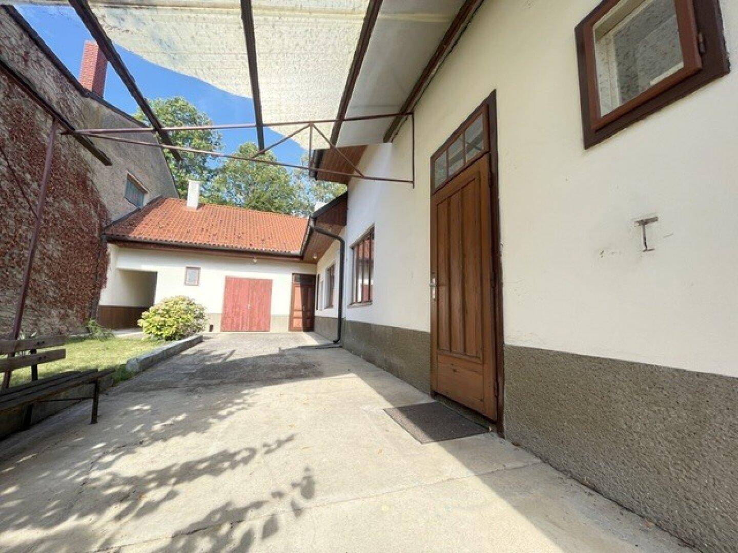 Überdachter Eingangsbereich im Innenhof mit Holztür und Blick auf das Nebengebäude.