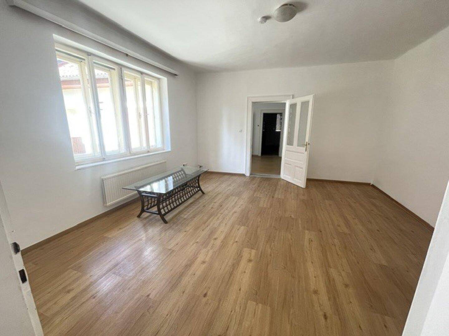 Helles Wohnzimmer mit Laminatboden, großen Fenstern und einem Couchtisch.