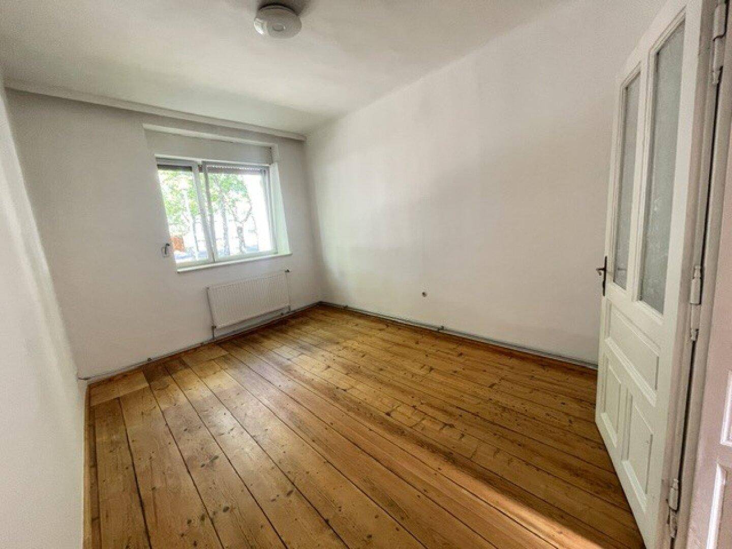 Helles Schlafzimmer mit Holzdielenboden, Fenster und weiß gestrichenen Wänden.