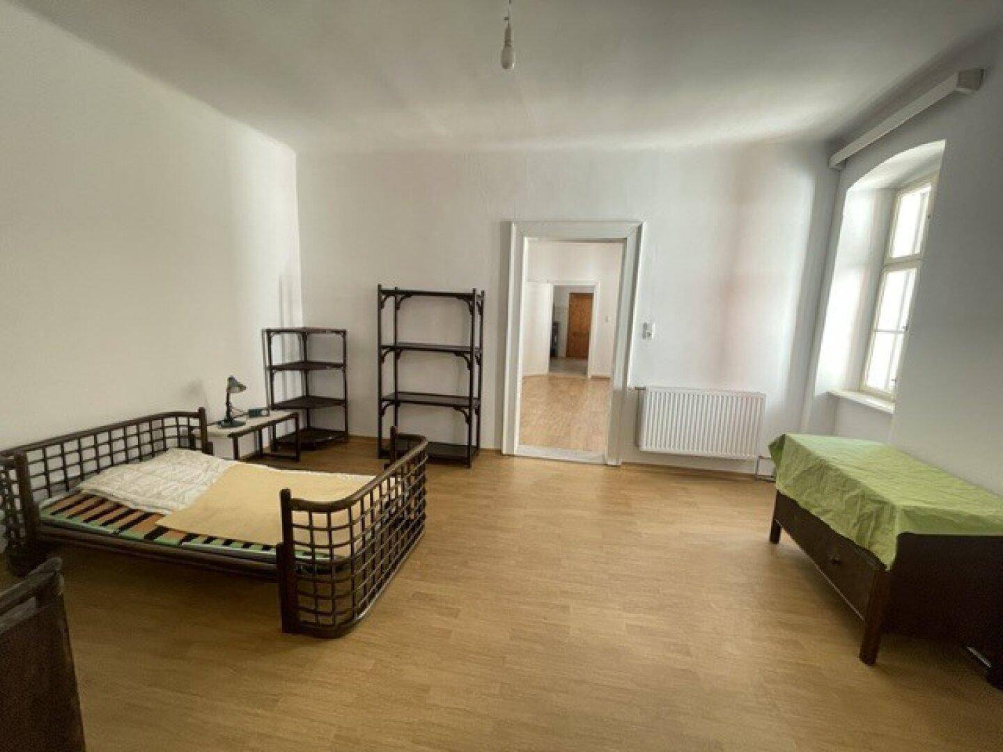 Schlafzimmer mit Holzbett, Regalen und Holzboden, bietet Zugang zu einem weiteren Raum.