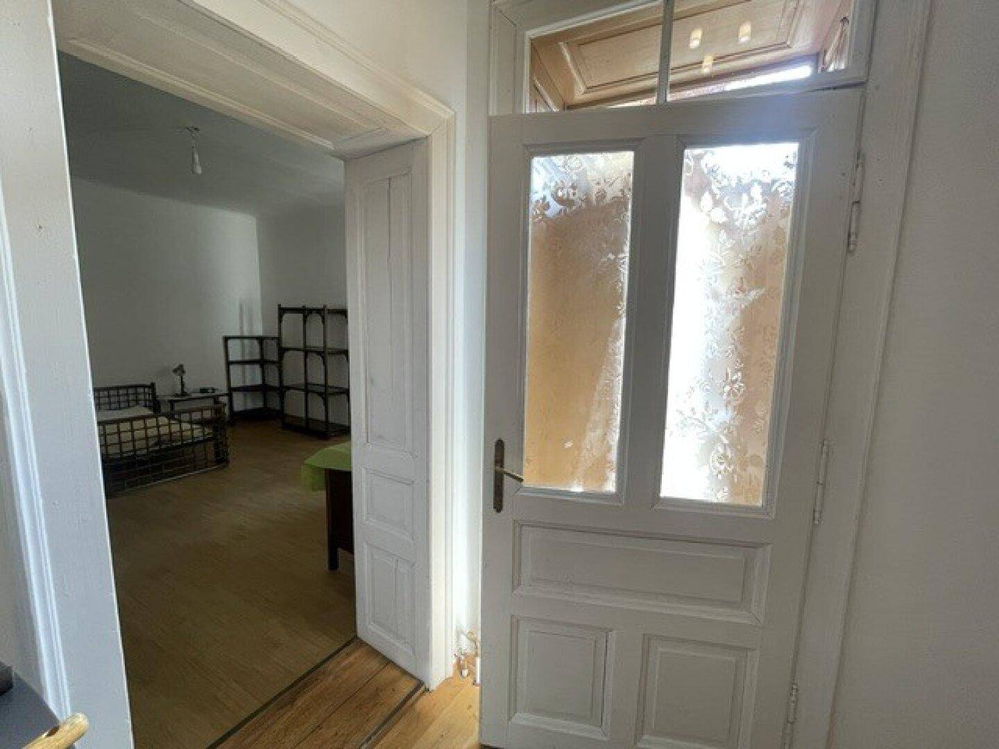 Innenansicht eines Flurs mit Holztür und Blick in ein angrenzendes Zimmer.
