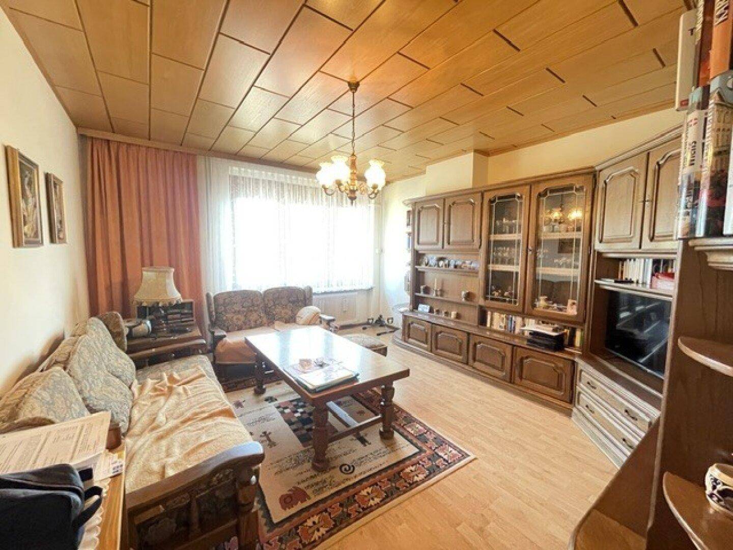 Gemütliches Wohnzimmer mit traditionellen Holzmöbeln, Parkettboden und Holzdeckenverkleidung.