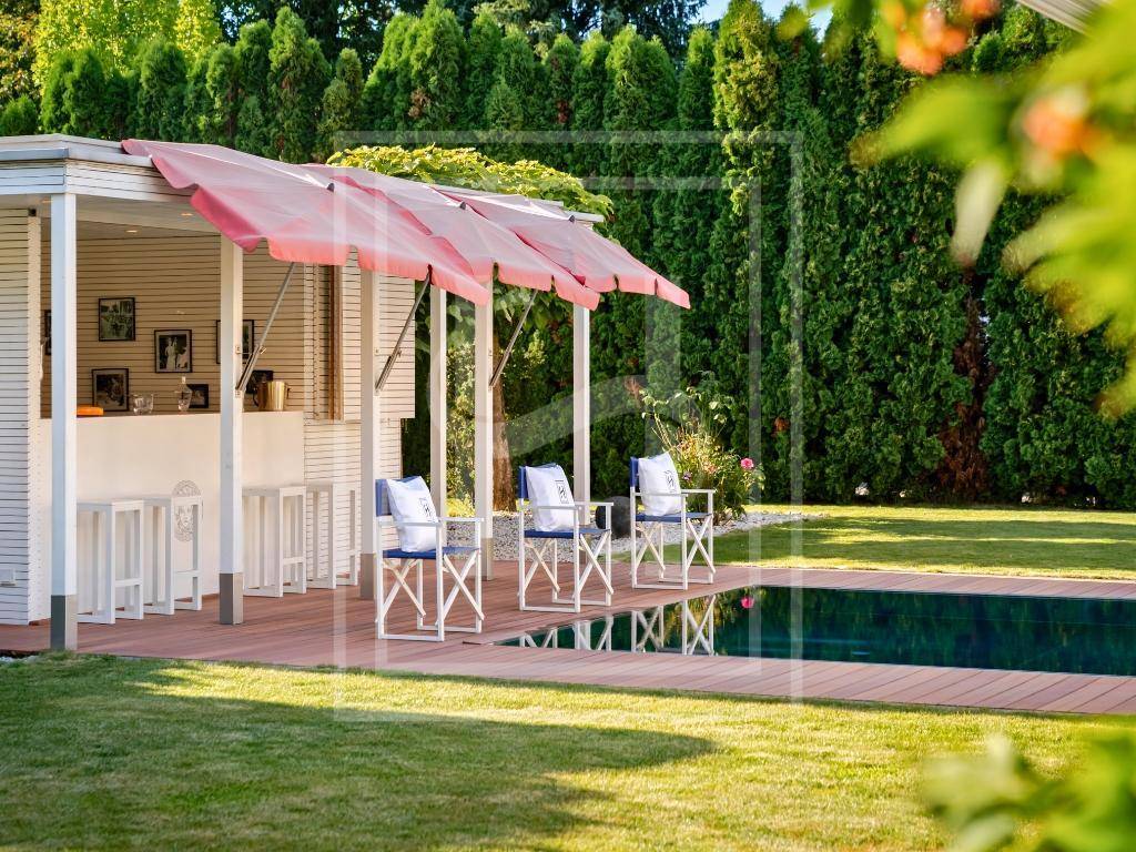 Gemütliche Poolbar mit Regiestühlen und roten Sonnenschirmen, direkt am Pool mit grüner Hecke.