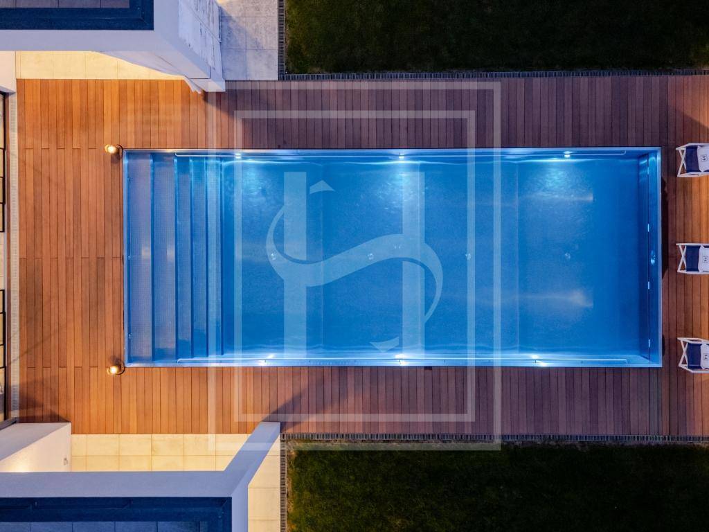Draufsicht auf den beleuchteten Swimmingpool und das Holzdeck bei Nacht, mit klaren Linien.