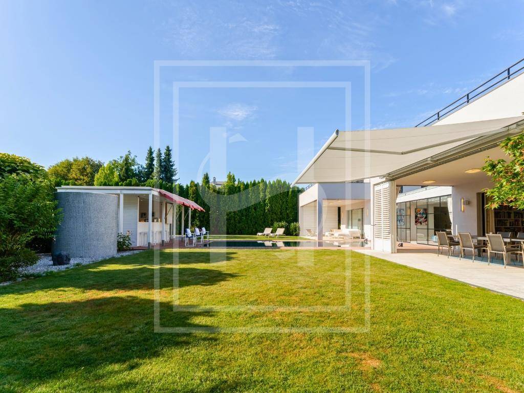 Weitläufiger Garten mit großer Rasenfläche, überdachter Terrasse und einem Poolbereich im Hintergrund.