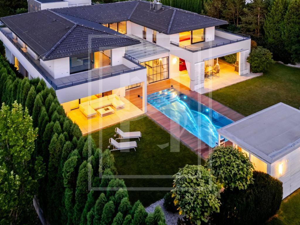 Beeindruckende Luftaufnahme einer modernen Villa mit beleuchtetem Pool und weitläufigem Garten bei Dämmerung.