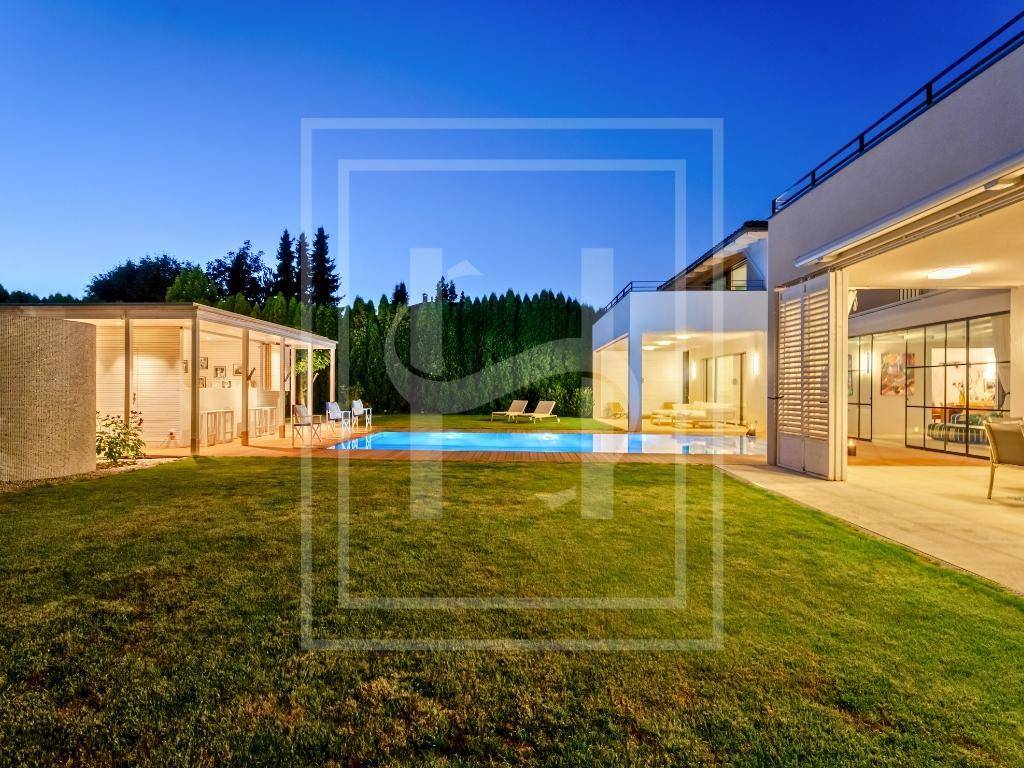 Weitläufiger Gartenbereich mit beleuchtetem Pool, Rasenfläche und einem charmanten Poolhaus bei Dämmerung.
