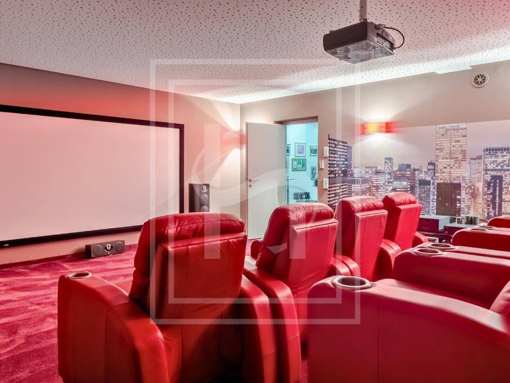 Exklusiver Heimkinoraum mit bequemen roten Ledersesseln, großer Leinwand und urbaner Wandgestaltung.