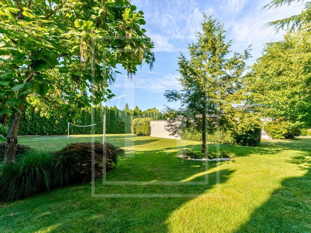 Weitläufiger, gepflegter Garten mit großen Bäumen, Rasenfläche und einem Volleyballnetz für Freizeitaktivitäten.