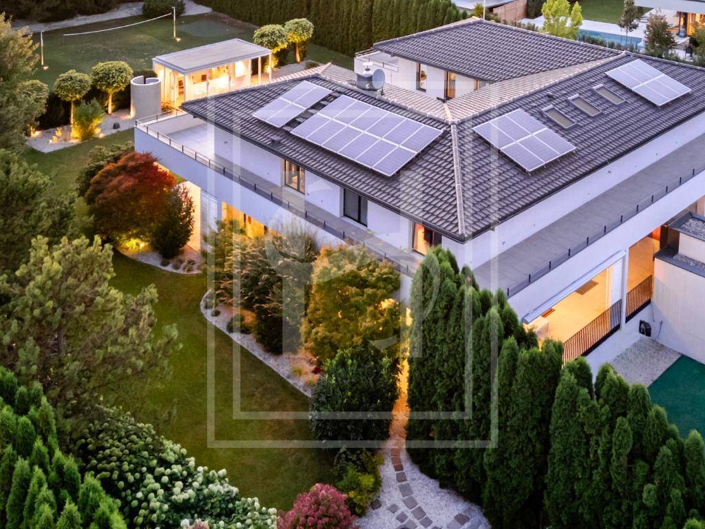Luftaufnahme einer modernen Villa mit Photovoltaikanlage auf dem Dach und einem gepflegten Garten.
