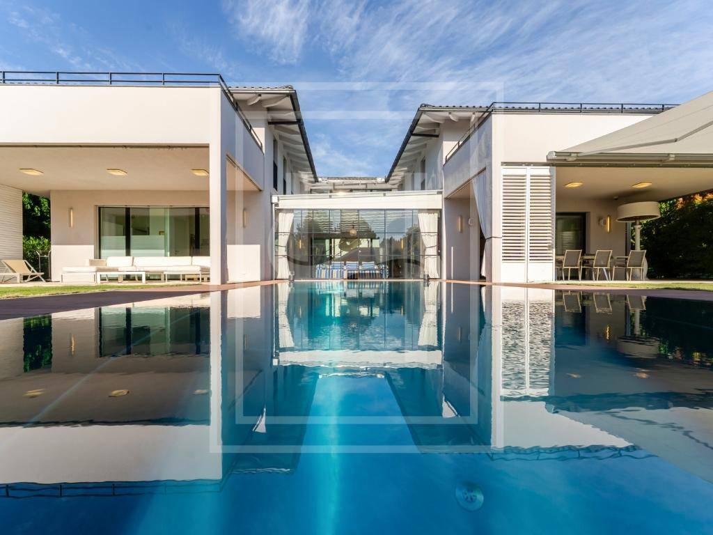 Moderne Villa mit großem Pool, der die Architektur und den blauen Himmel widerspiegelt.
