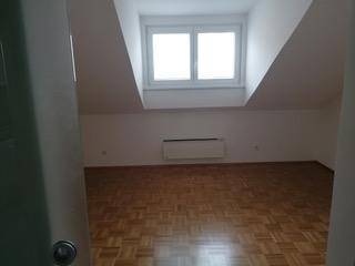 Heller Raum im Dachgeschoss mit Dachschrägen, Parkettboden und großem Fenster.