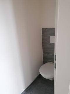 Kleines Gäste-WC mit Wand-WC und grauen Fliesen an der Wand.