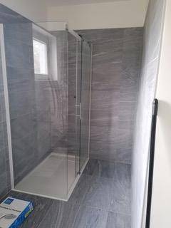 Modernes Badezimmer mit großer begehbarer Dusche und grauen Fliesen.