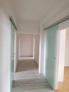Heller Flur mit modernen Glasschiebetüren und hellem Laminatboden.