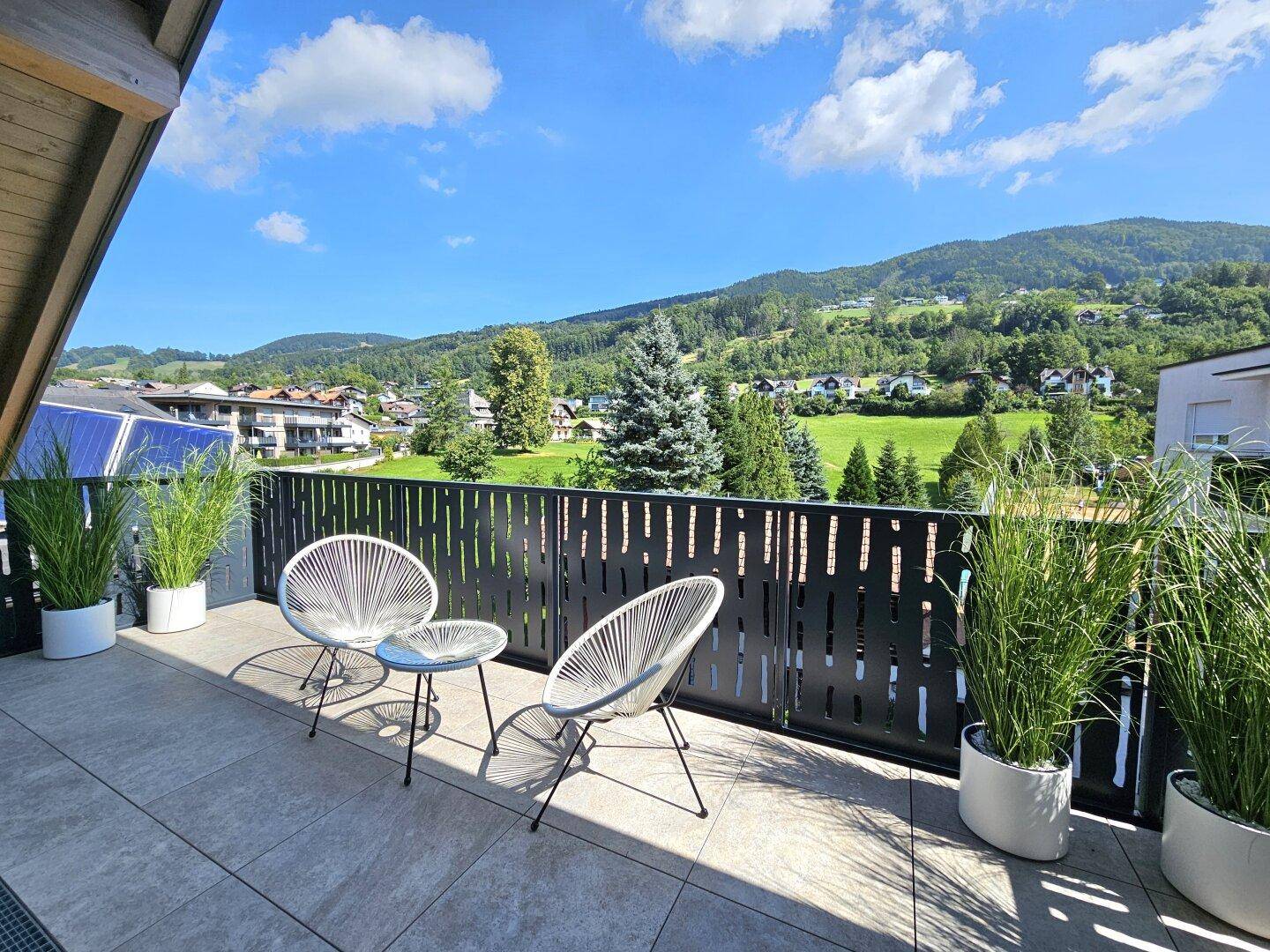 Sonniger Balkon mit Sitzgelegenheiten und weitem Blick auf die grüne Berglandschaft.