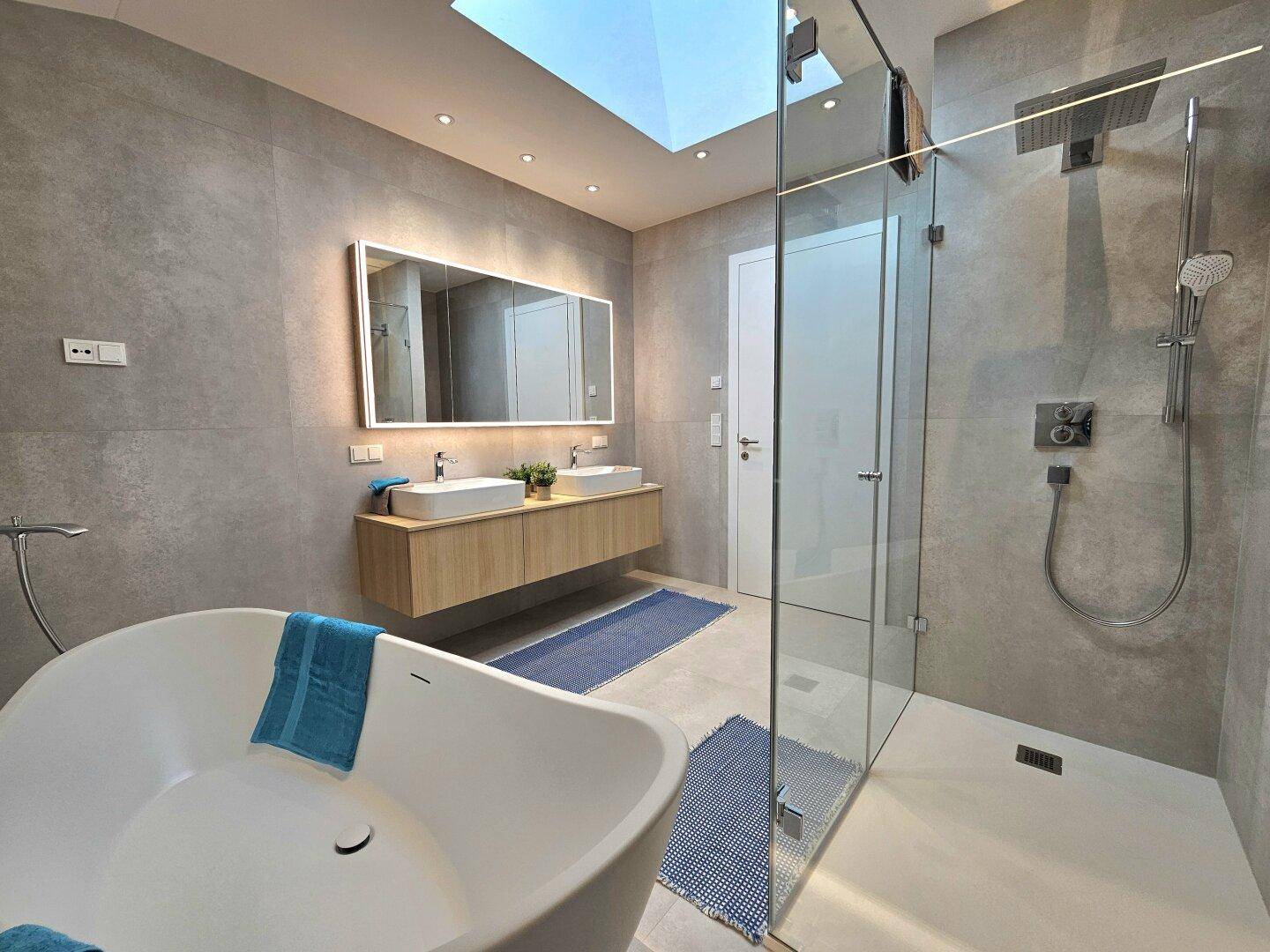 Elegantes Badezimmer mit großer Dusche, freistehender Badewanne und Doppelwaschbecken unter dem Dachfenster.