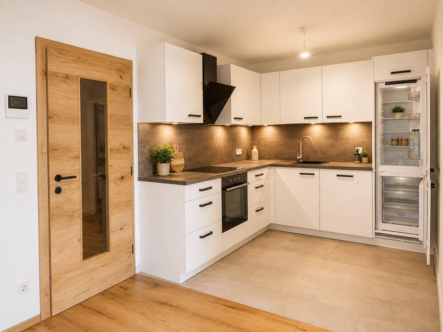 Moderne Einbauküche mit weißen Schränken, dunkler Arbeitsplatte und integrierten Geräten, angrenzend an Holzboden.