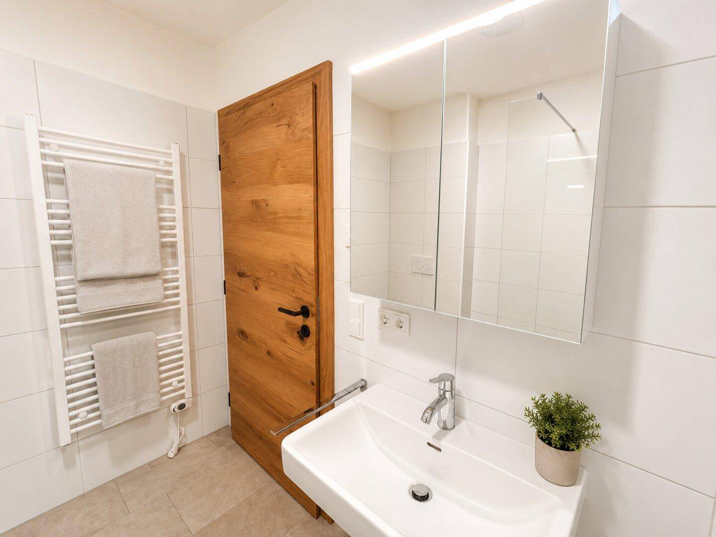 Modernes Badezimmer mit Einzelwaschbecken, Spiegelschrank, beheiztem Handtuchhalter und weißen Fliesen.