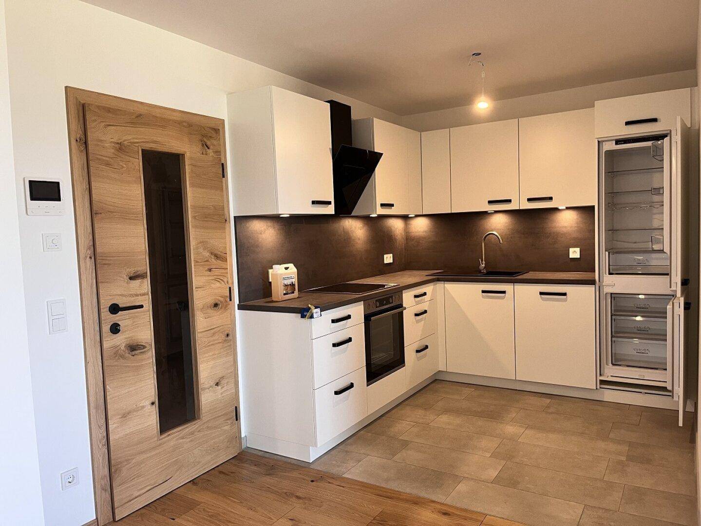 Moderne Einbauküche mit weißen Schränken, dunkler Arbeitsplatte und integrierten Geräten, angrenzend an Holzboden.