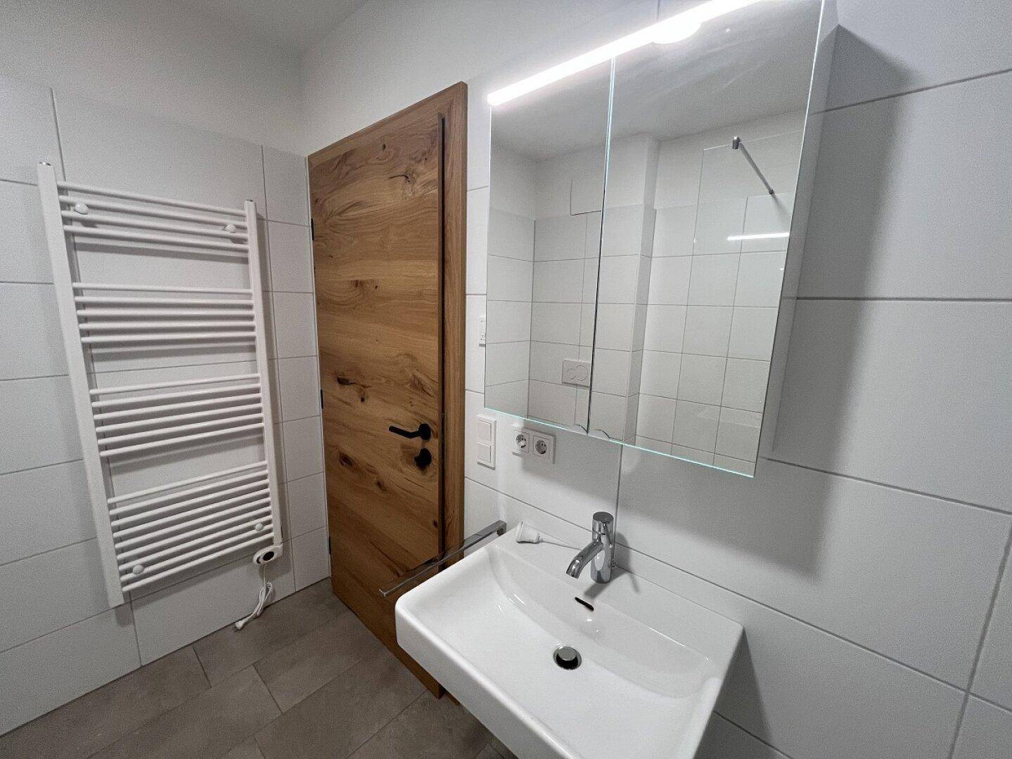 Modernes Badezimmer mit Einzelwaschbecken, Spiegelschrank, beheiztem Handtuchhalter und weißen Fliesen.