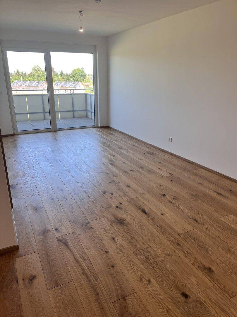 Geräumiges Wohnzimmer mit Holzboden und großen Schiebetüren zum Balkon mit grüner Aussicht.