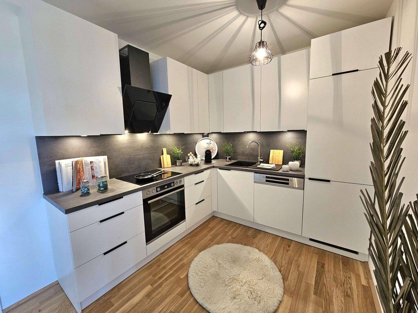 Moderne Einbauküche mit weißen Schränken, dunkler Arbeitsplatte und Holzboden.