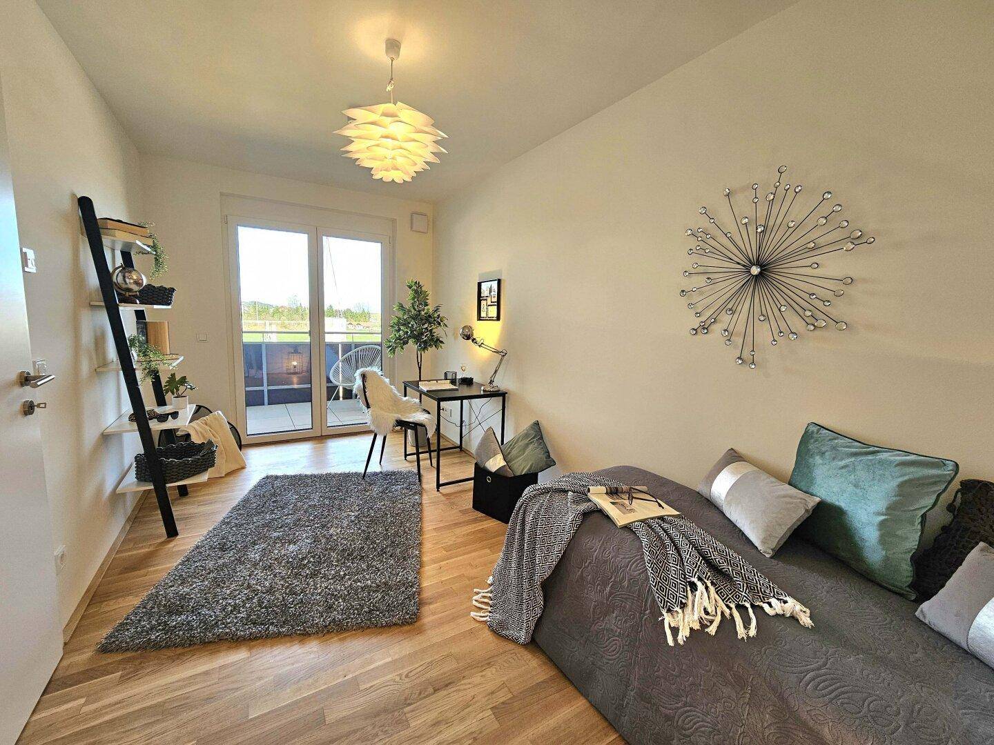 Helles Zimmer mit Schreibtisch, Regal und Zugang zu einem kleinen Balkon.