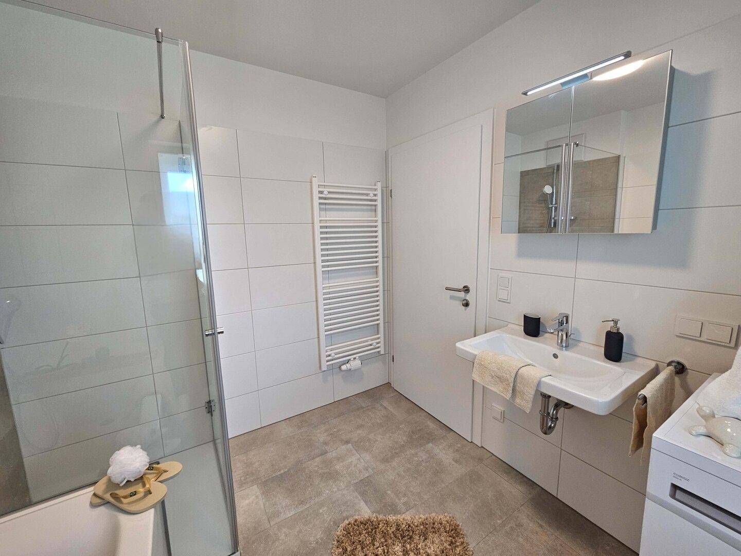 Modernes Badezimmer mit Dusche, Waschbecken und weiß gefliesten Wänden.