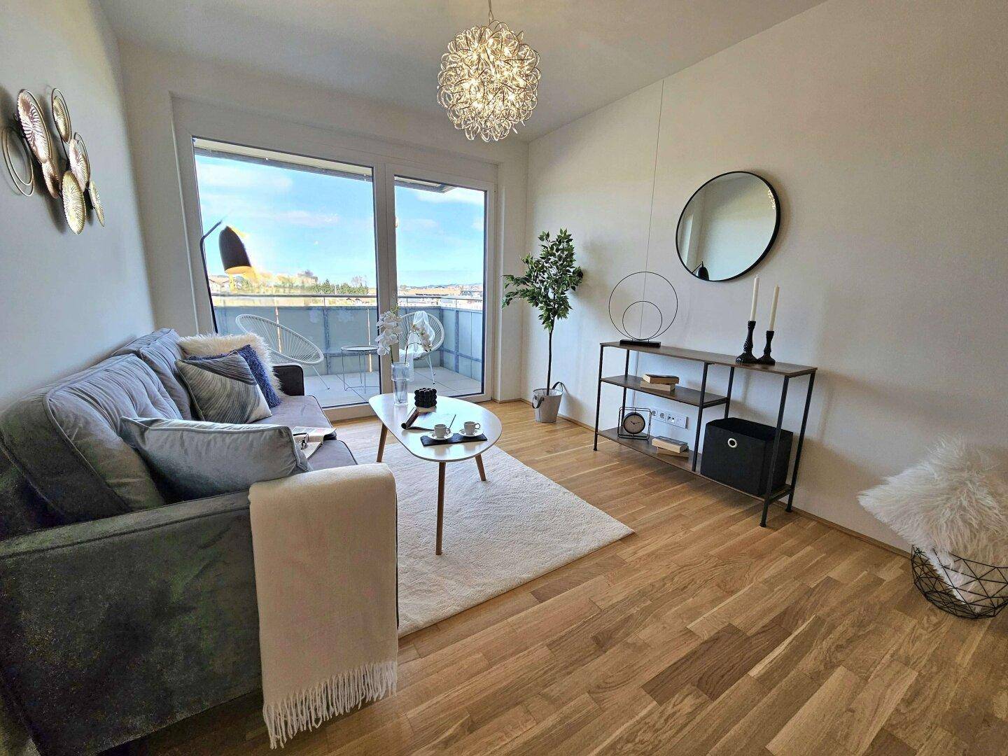 Helles Wohnzimmer mit Holzboden, modernem Sofa und Zugang zu einem Balkon.
