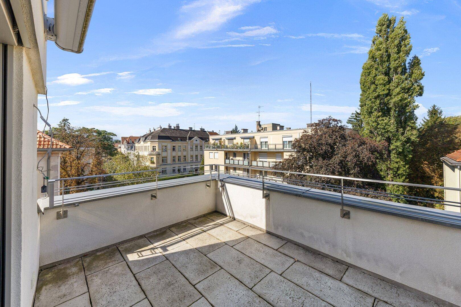 Sonniger Balkon mit Steinplattenboden und weitem Blick über die umliegende Stadtlandschaft.