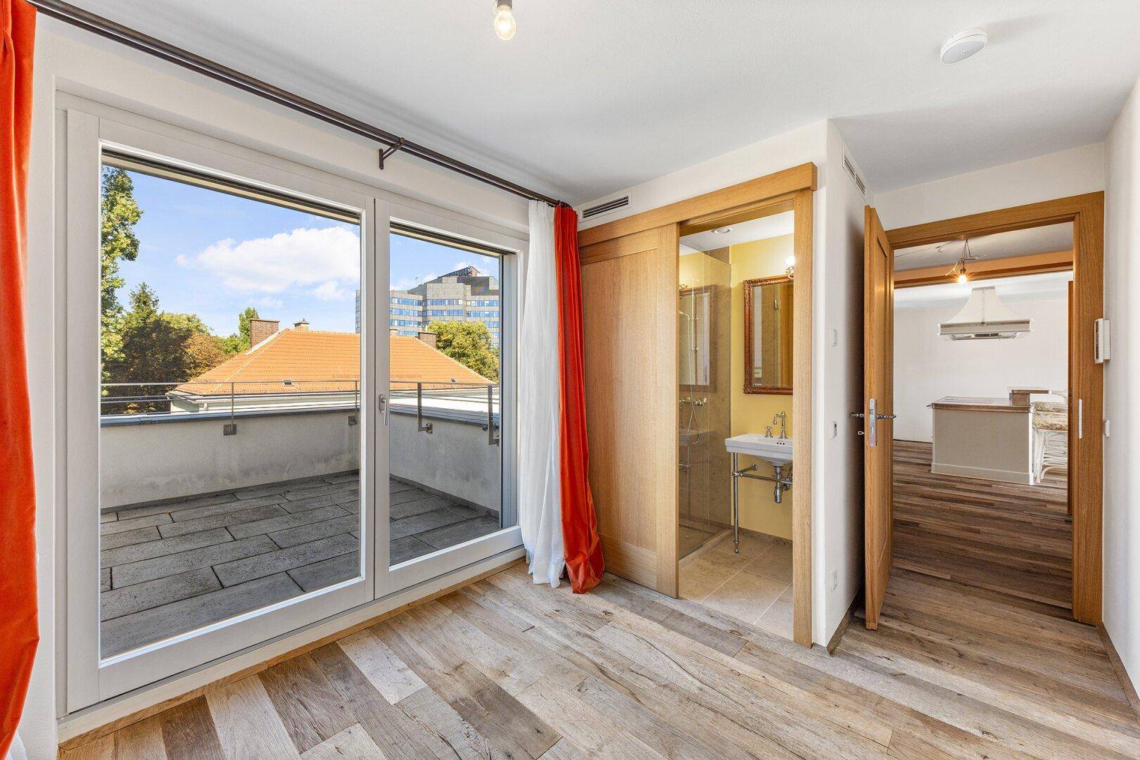 Schlafzimmer mit Holzboden, großem Balkonzugang und direktem Zugang zu einem Badezimmer.