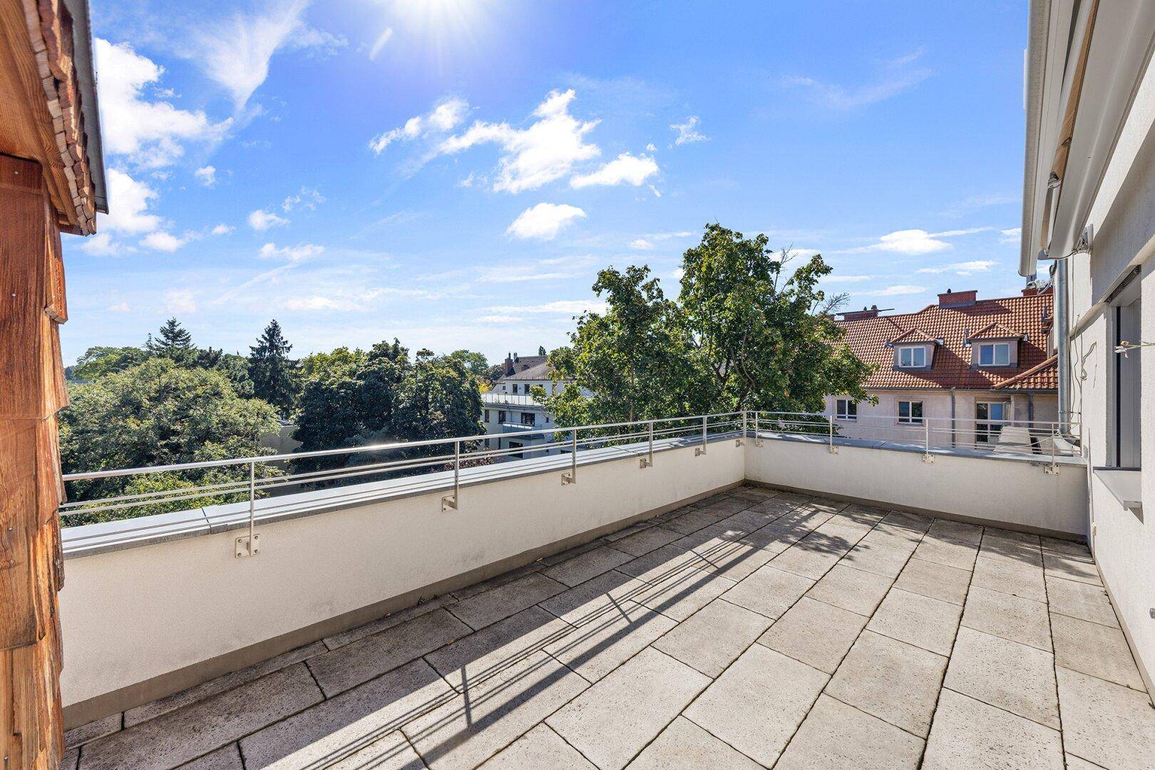Weitläufige Dachterrasse mit Steinplatten und sonnigem Ausblick über die Dächer der Stadt.